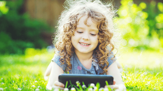 Kid playing with tablet lying on grass